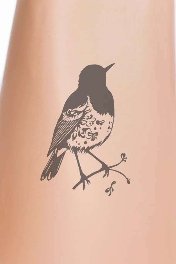 Close-up of a person's calf featuring a temporary temporary tattoo. The temporary tattoo showcases a stylized black and white illustration of a bird perched on a simple branch. The bird, facing right with its wings spread and body angled, has its head turned left and be