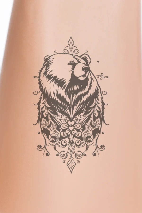 Close-up of a person's calf featuring a temporary temporary tattoo of a bear's head and neck in bold black and white. The bear, facing right with closed eyes, showcases intricately detailed fur patterns, swirling lines, and floral elements. Its expressive face includes