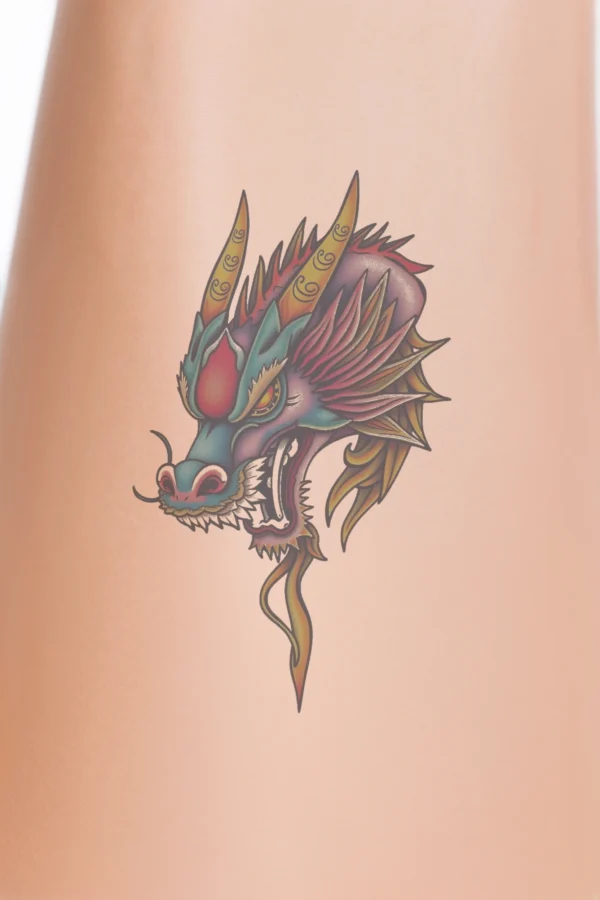 Close-up of a person's calf featuring a vibrant dragon temporary tattoo. The dragon's head, illustrated in traditional temporary tattoo style, dominates the design with its fierce expression and open mouth displaying sharp teeth. The body is a blend of blue and purple, accented by bright