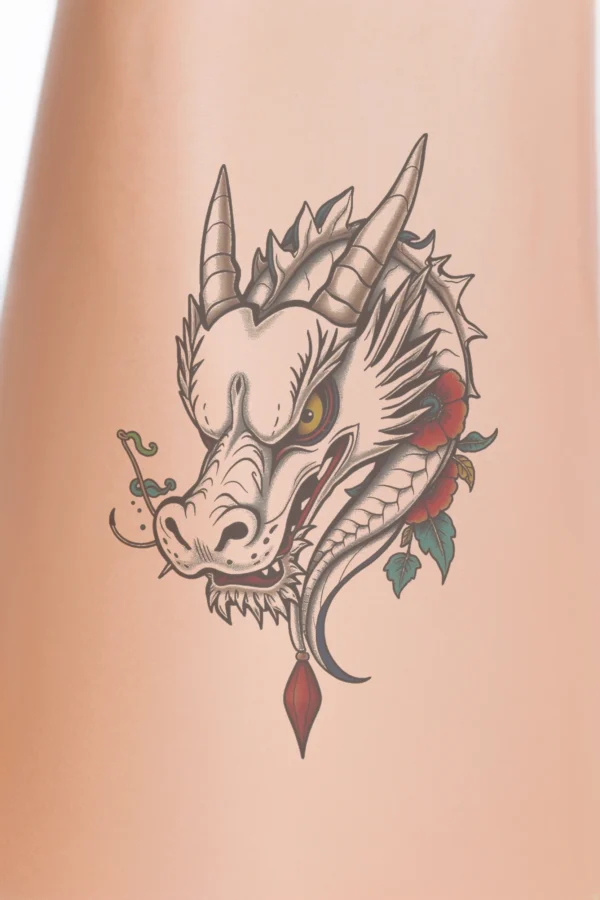 Close-up of a person's lower leg showcasing a temporary temporary tattoo on the calf. The temporary tattoo features a dragon's head in profile, illustrated in a traditional Japanese style. The dragon is predominantly white with black and gray accents, displaying a prominent red eye and an