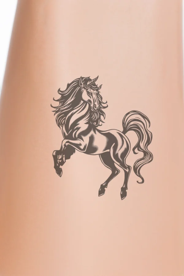Close-up of a person's calf featuring a temporary temporary tattoo of a majestic dark horse rearing up on its hind legs. The horse has a flowing, stylized mane and tail, emphasizing its dynamic movement. Its head is turned to the left, with its