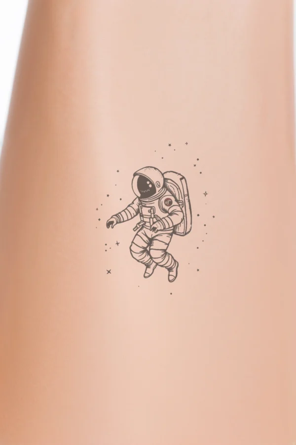 A black and white temporary temporary tattoo design featuring an astronaut in a white spacesuit and a dark helmet, floating in space. The astronaut is centrally positioned, with bent knees and arms extended sideways, conveying a sense of motion. A red patch on the shoulder