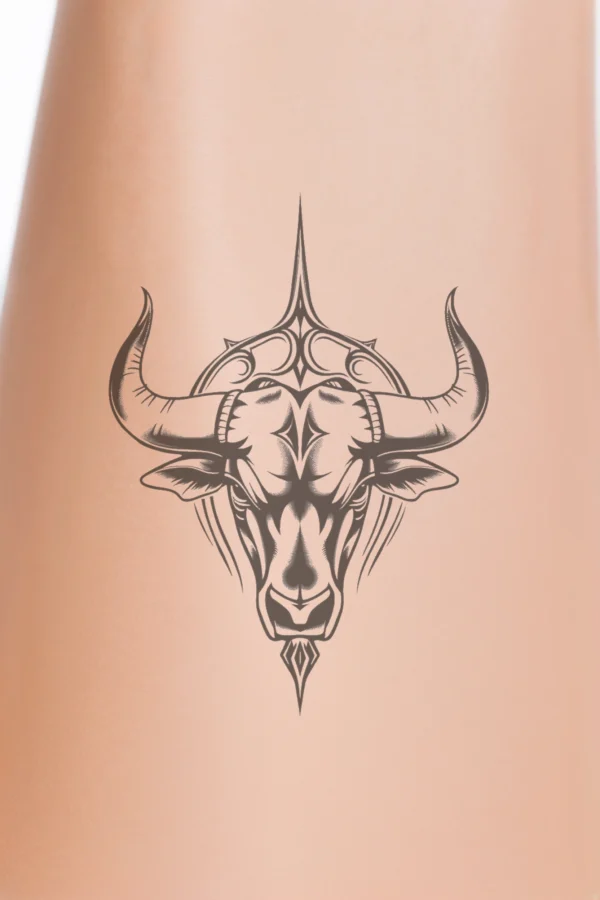 Black and white temporary temporary tattoo design featuring a prominent bull's head facing right. The bull's head showcases a large, detailed horn on the left and a smaller horn on the right, with intricate patterns on its face, including a bold eye and a defined