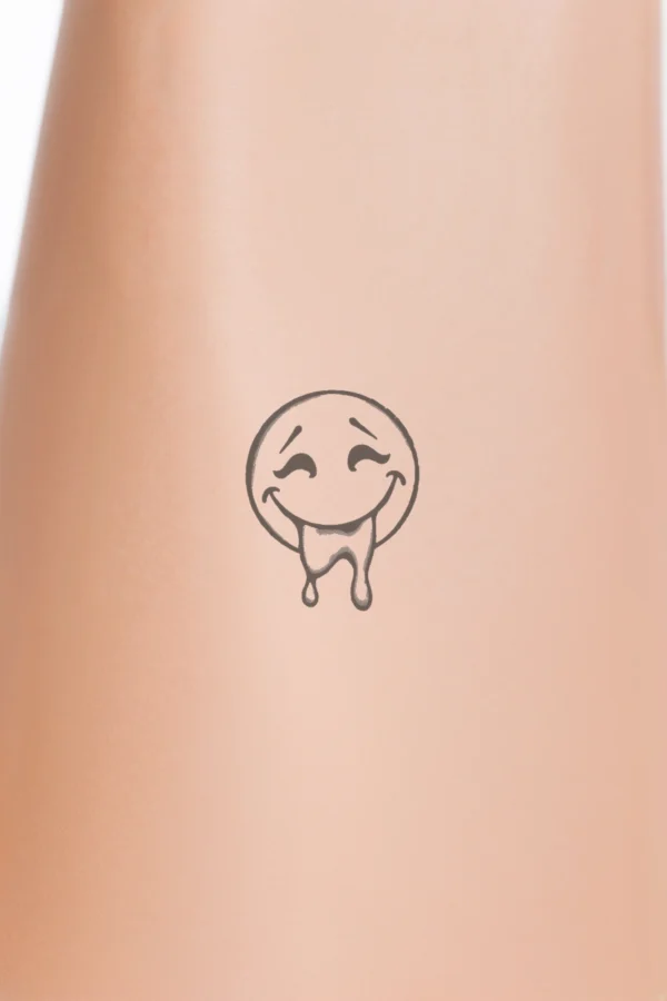 Temporary temporary tattoo featuring a simplistic black and white drawing of a smiling face. The design includes a top half that is an oval shape with a curved line for the mouth, and a bottom half that is another oval with a smiley curve. The eyes are