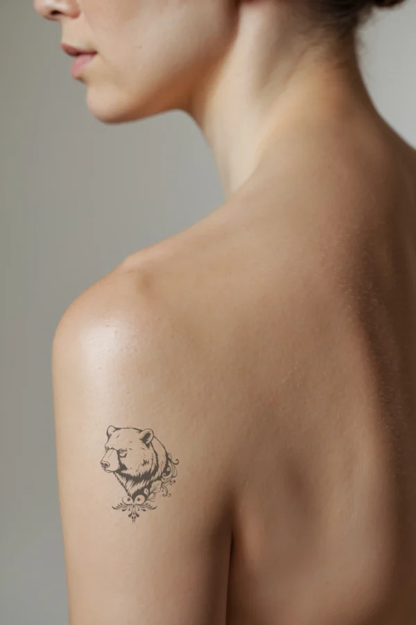 A profile view of a person's shoulder showcasing a striking black and white temporary temporary tattoo. The design features a detailed illustration of a bear's head turned to the left, with thick, textured fur and dark eyes gazing directly at the viewer. The bear's