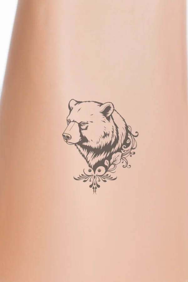 A temporary temporary tattoo design featuring a detailed black and white illustration of a bear's head and shoulders, facing left. The bear's thick, textured fur is predominantly dark, with a lighter black nose and intense dark eyes gazing directly at the viewer. Its