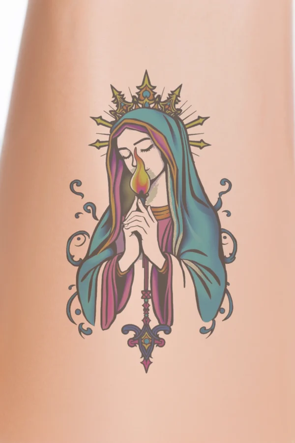 Close-up of a person's lower legs featuring a colorful temporary temporary tattoo on the calf. The temporary tattoo depicts a stylized Virgin Mary wearing a blue robe and a pink veil, crowned, with her hands clasped in prayer and holding a lit candle in her right
