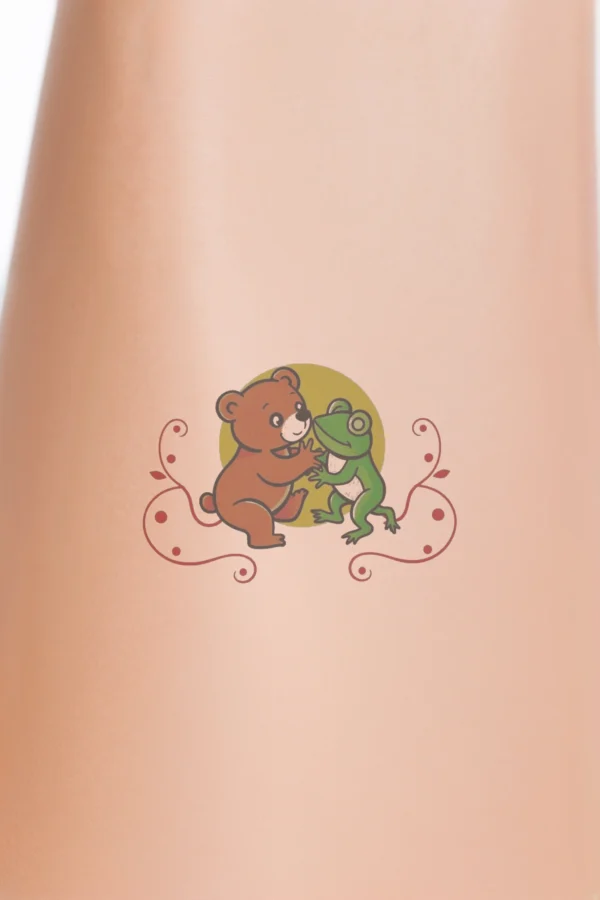 A colorful temporary temporary tattoo design featuring a friendly interaction between a reddish-brown bear and a green frog. The bear, sitting on its hind legs, faces the frog, which stands on its hind legs in return. They are set against a yellow circular background