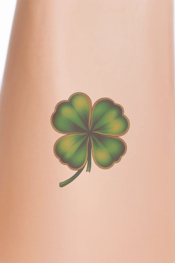 A vibrant temporary temporary tattoo design featuring a four-leaf clover in green and orange. The clover's four distinct leaves are symmetrically arranged, with green leaves forming the main body and contrasting orange stems. Set against a stark white background, the
