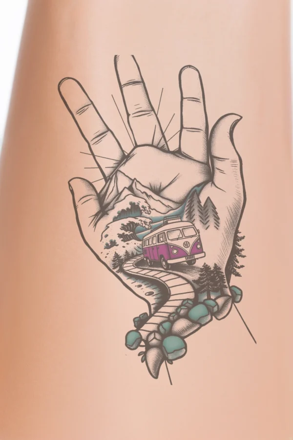 A hand featuring a temporary temporary tattoo of a pink and white Volkswagen van on the palm, surrounded by a whimsical landscape scene of mountains, a winding road, and a small dark tree. The design showcases stylized artwork with a vibrant color palette primarily consisting of
