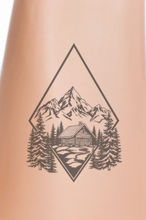 A striking black and white temporary temporary tattoo design features a realistic mountain range with detailed peaks and valleys, set against a clear sky. The illustration includes a small cabin nestled in the valley, surrounded by stylized trees, along with a winding path leading to the